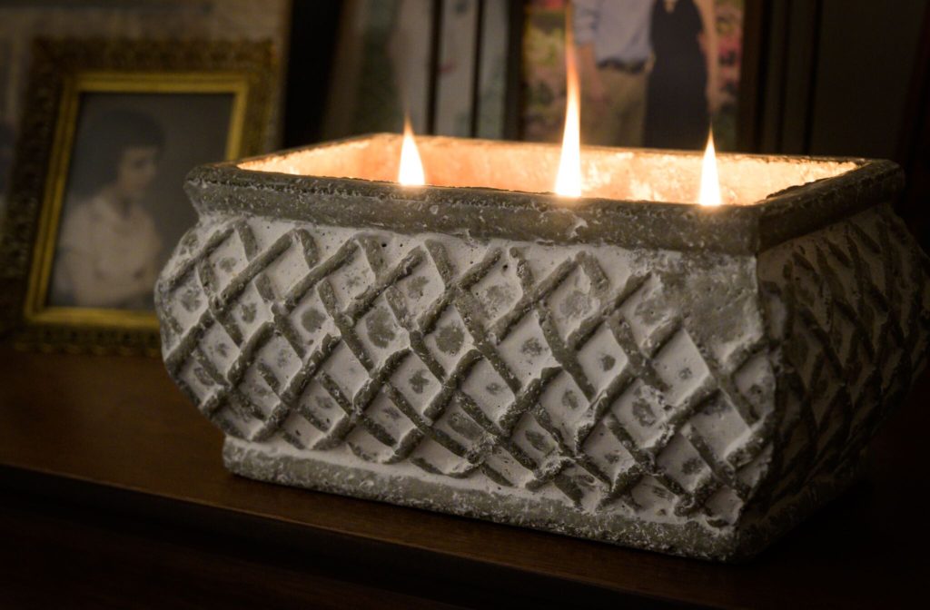 Picture of a lite brick candle with a check pattern in gray and distressed white. The candle is sitting on a side table with an antique photograph behind it. This photo is showing that candles are an inexpensive teacher's gift.