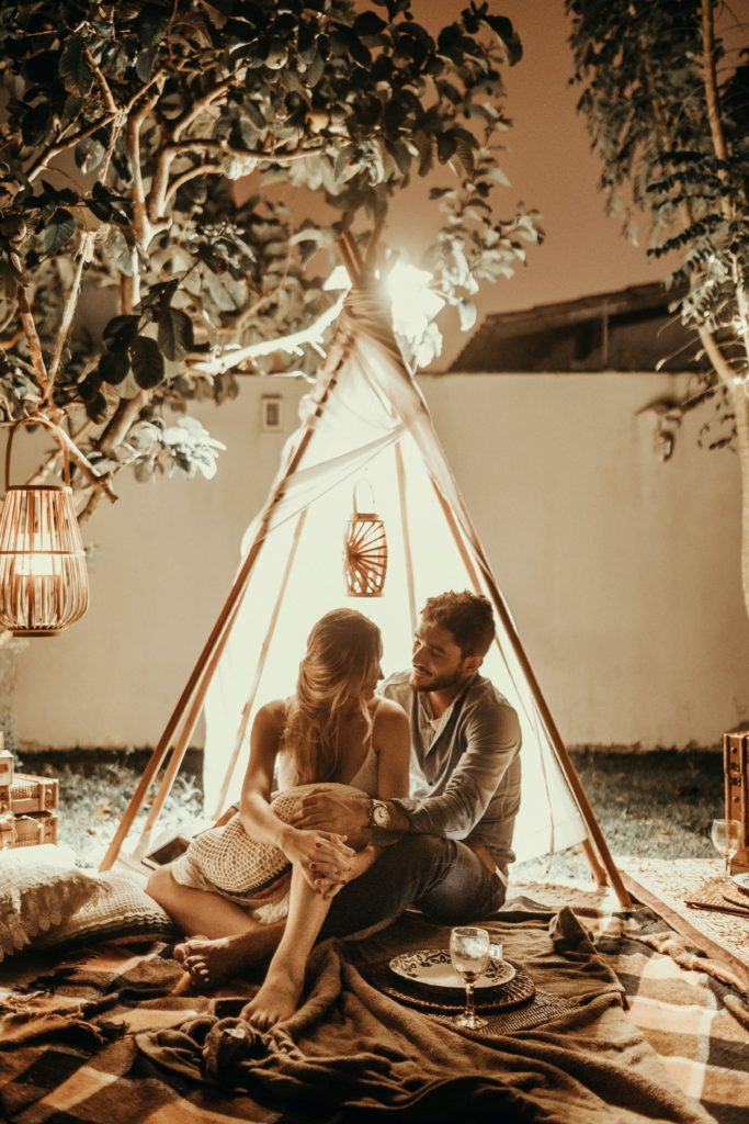 Couple outside in a tent enjoying wine by lanterns. This romantic date night idea can happen right in your back yard.