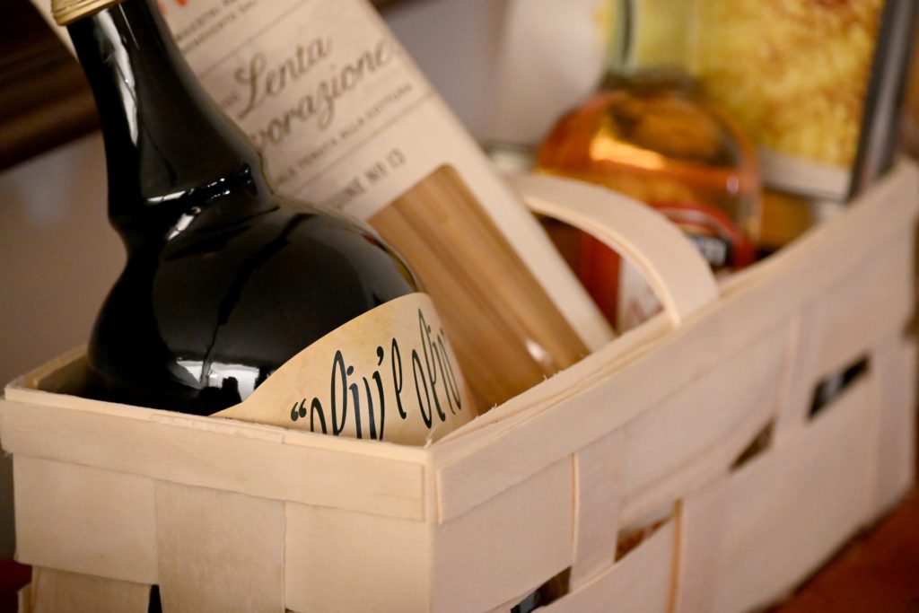 Rectangle wooden gift basket filled with olive oil, noodles and a few to things that are blurred out. Photograph is taken in portrait mode.