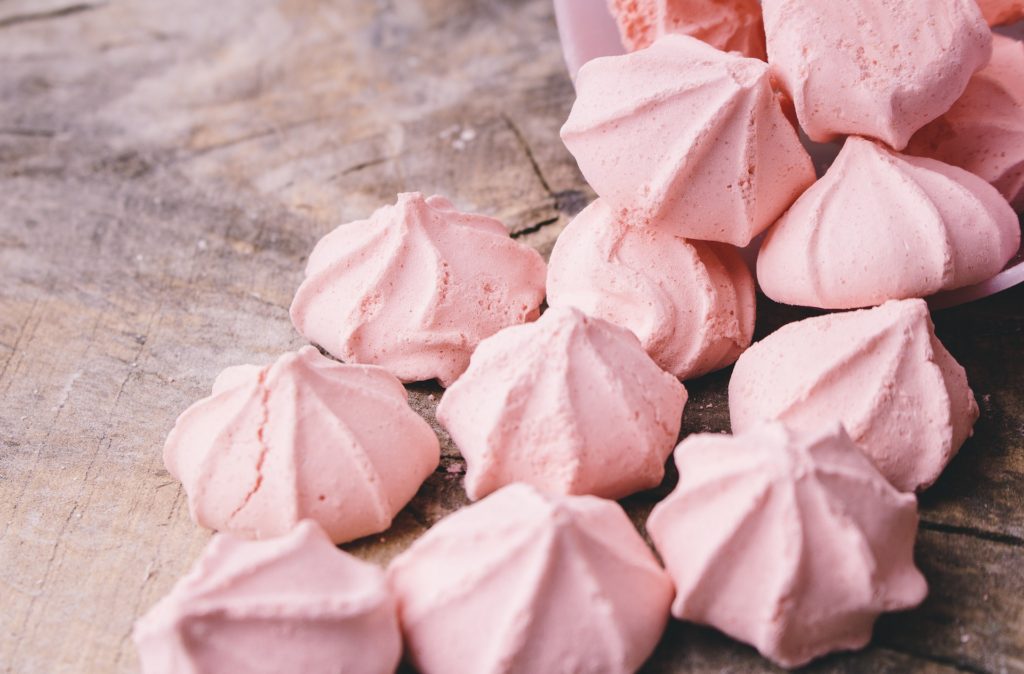 Picture is of small pale pink meringue candies on a rustic wooden table.