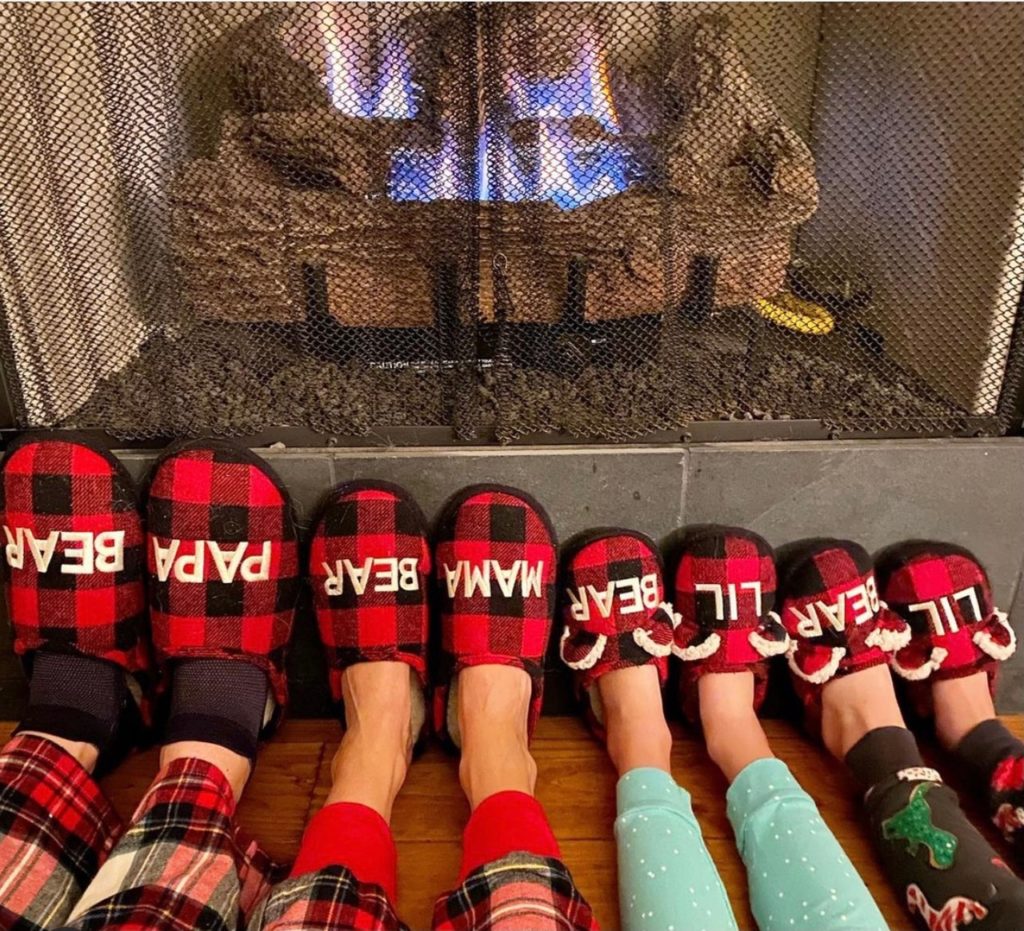 Family's feet by the fire in Christmas slippers.